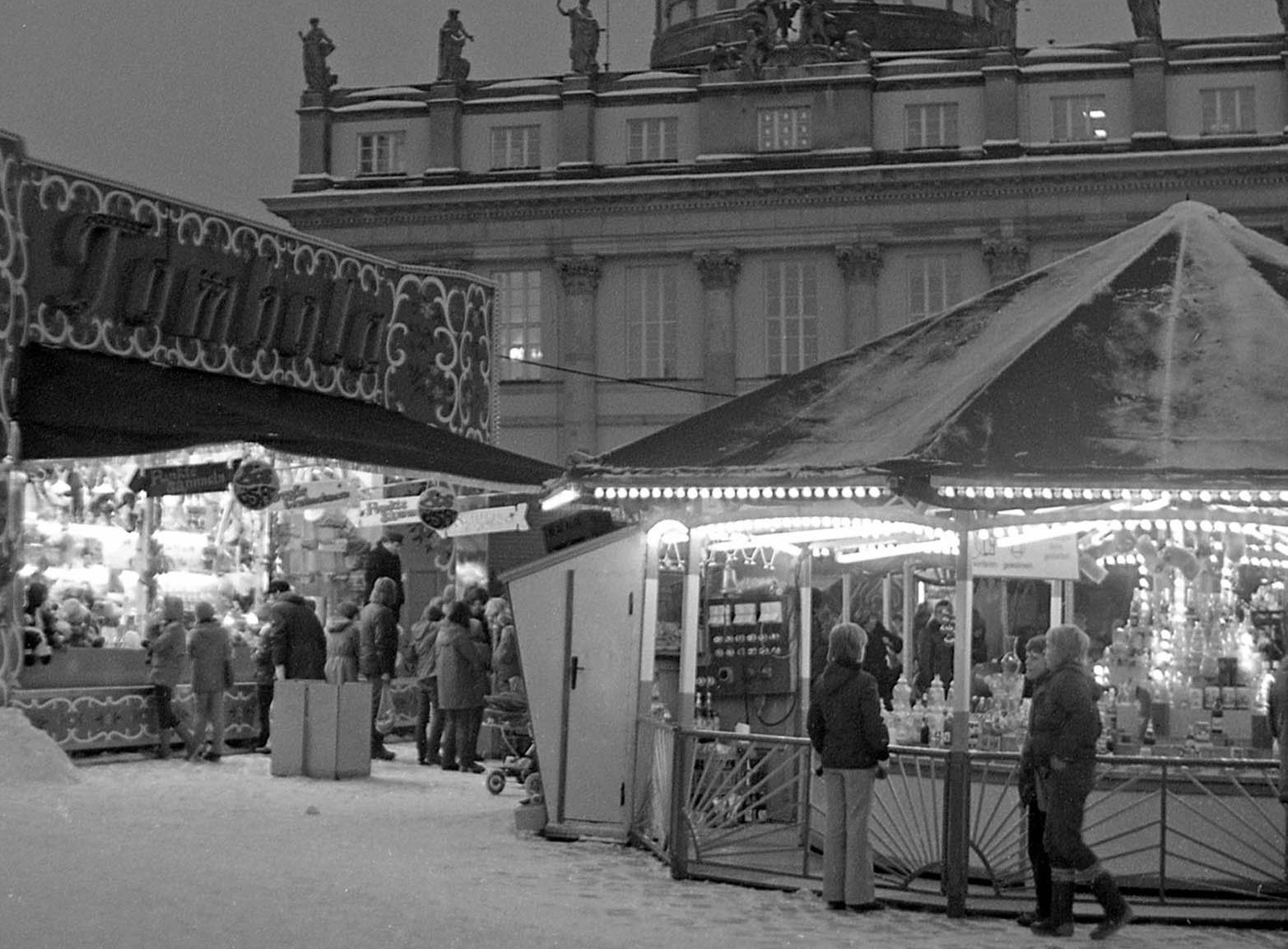 Foto: Weihnachtsmarktbuden vor dem Alten Rathaus in Potsdam. Im Vordergrund beleuchtete Buden und im Hintergrund ist das Rathaus zu sehen.