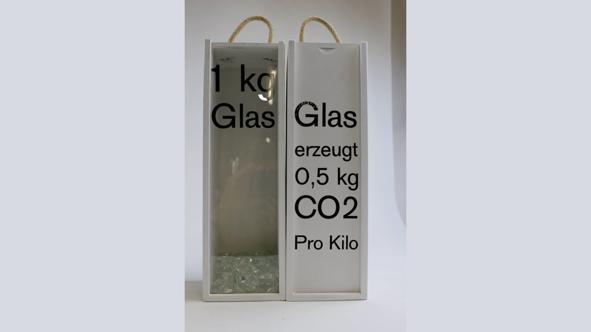 Foto: Zwei Behälter mit Aufschrift, auf dem Einen steht "1kg Glas" und auf dem Anderen "Glas erzeugt 0,5kg CO2 pro Kilo"